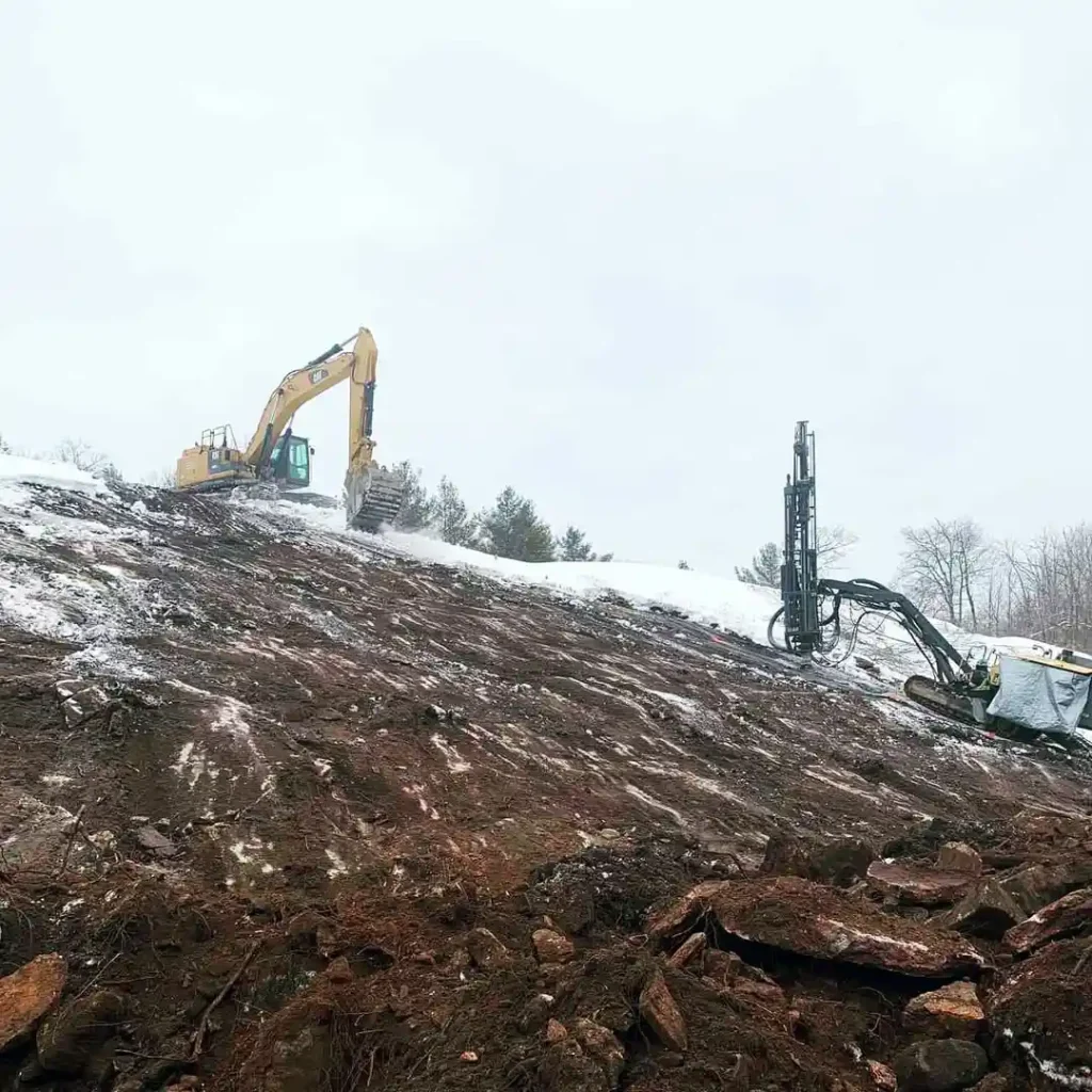 Track excavator and drilling equipment performing winter rock excavation in Ontario
