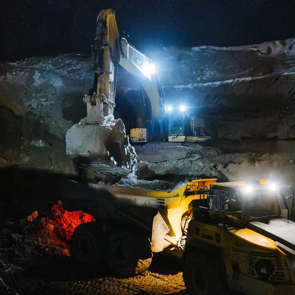 Heavy excavator and haul truck performing night operations at Northern Ontario mining site with safety lighting